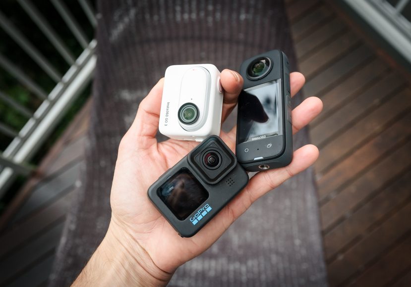 A person holding two action cameras on a deck.