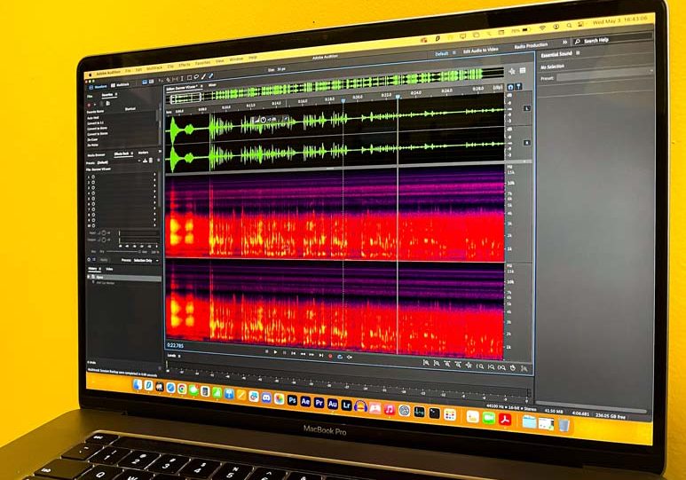 A macbook screen showing the waveform view of an audio file in adobe audition with a yellow background