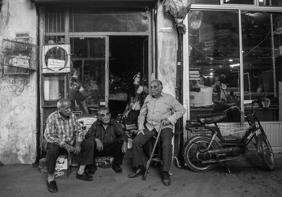 a group of men sitting in front of a shop.