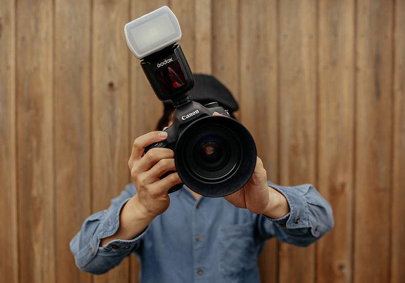 a person holding a camera with flash diffuser attached up to their face.