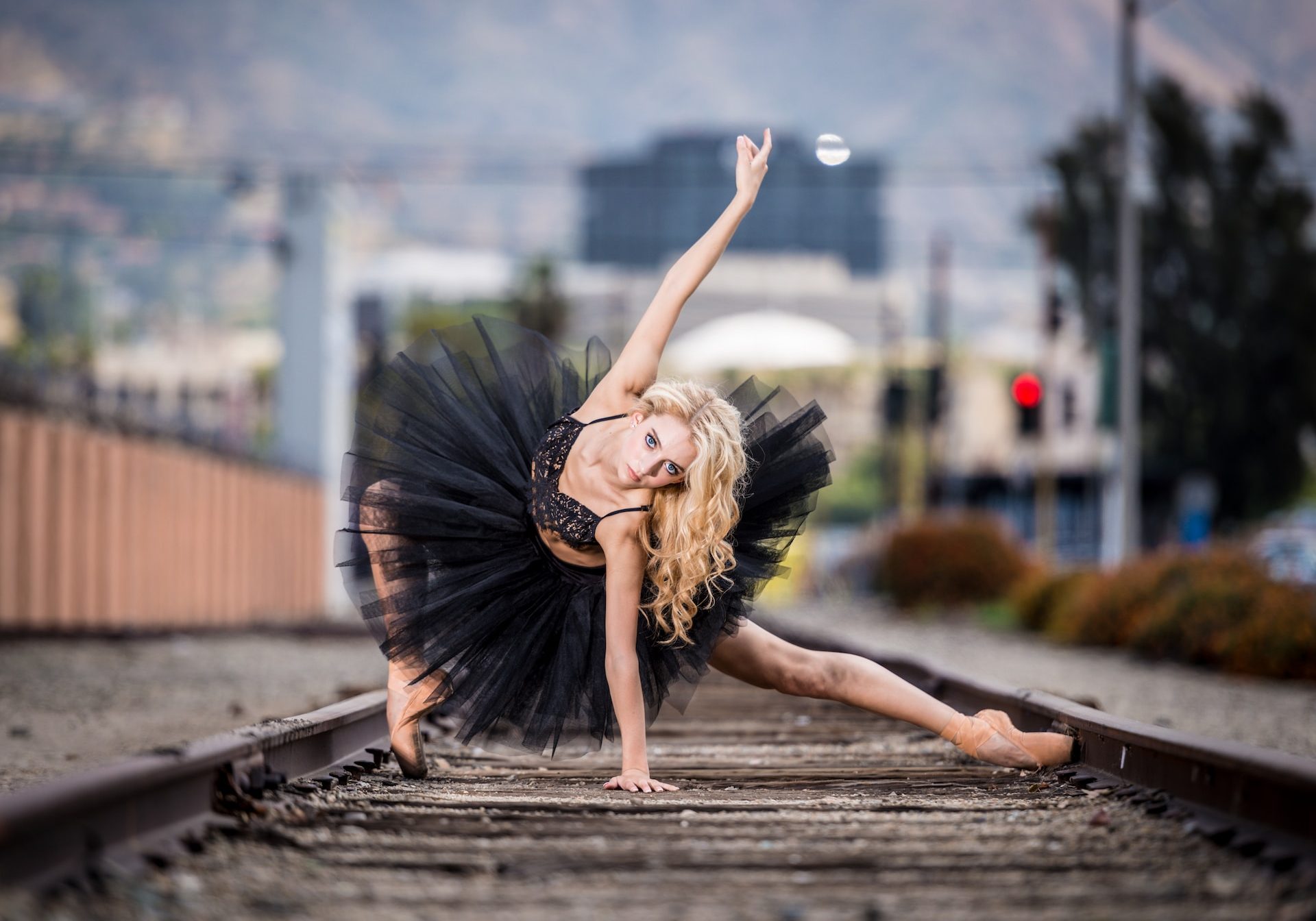 A young woman in a black tutu is posing on railroad tracks.