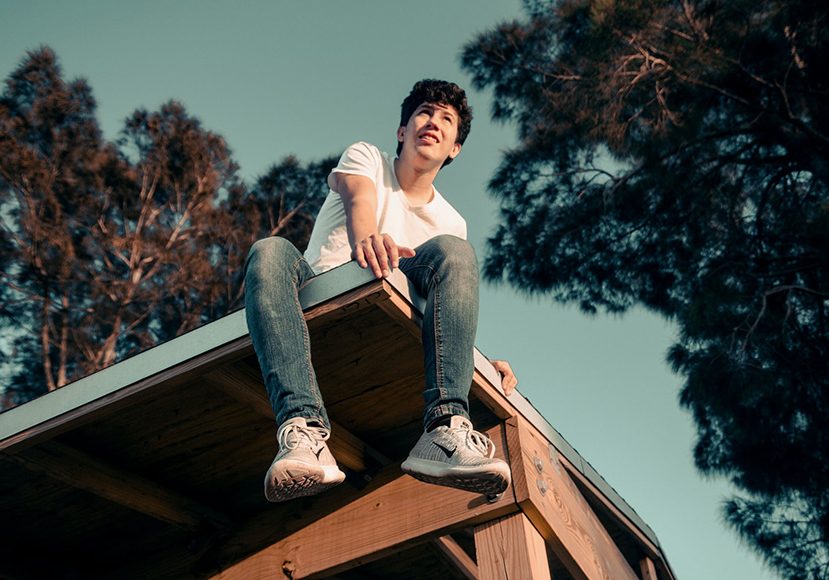 a young man sitting on top of a wooden structure.