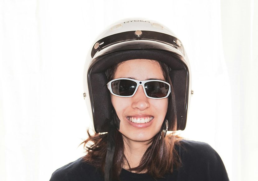 Woman with a smile wearing sunglasses and a motorcycle helmet.