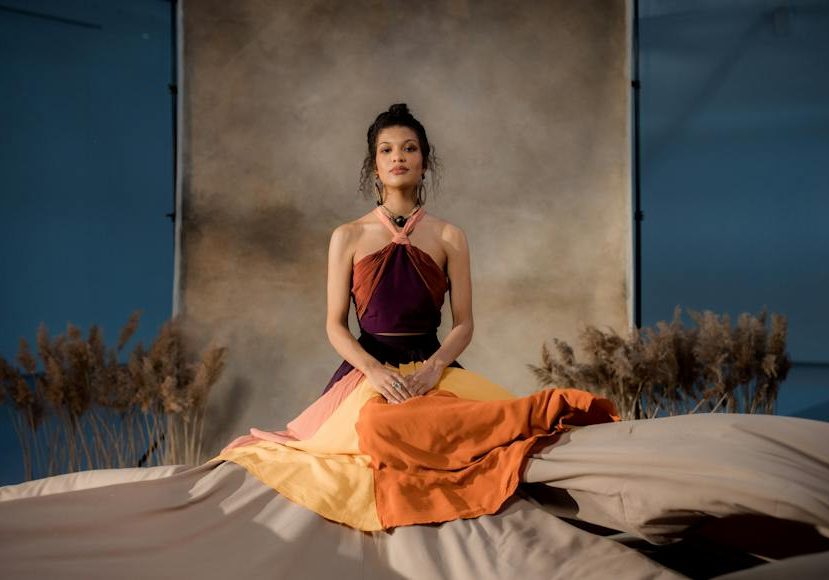A woman in a colorful dress sitting on a bed.