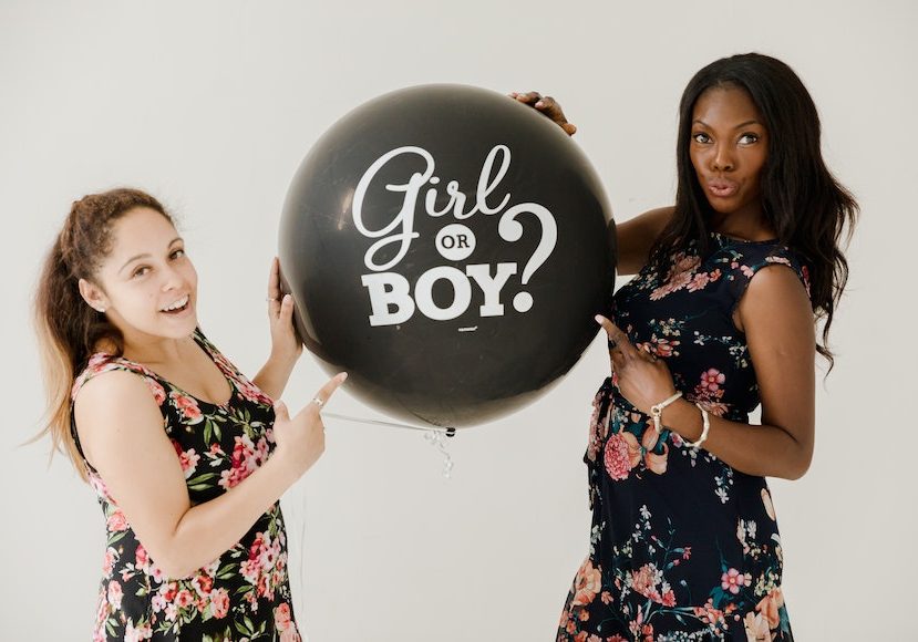 two women holding a balloon that says girl or boy.