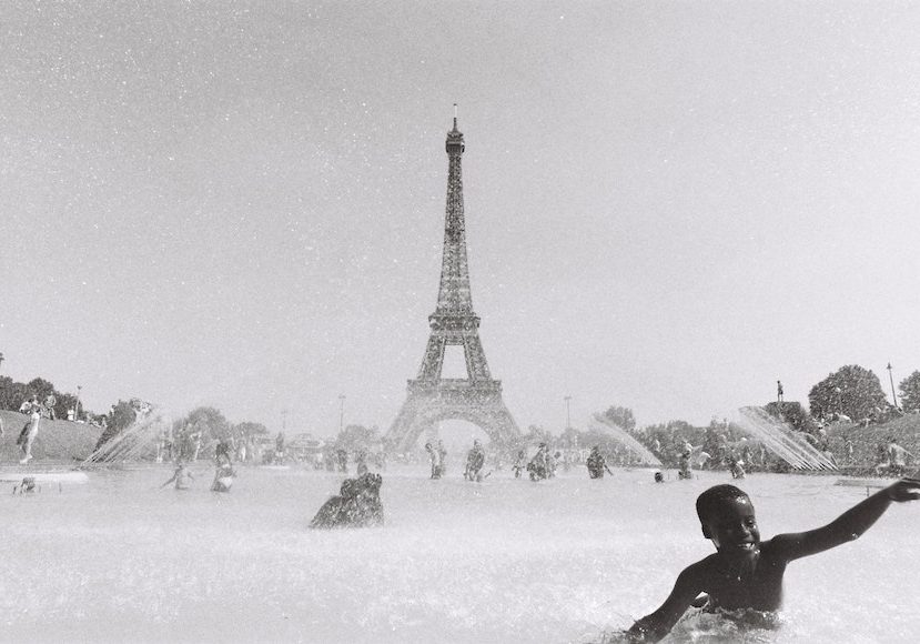Black and white photo of a boy playing in a fountain with the eiffel tower in the background.