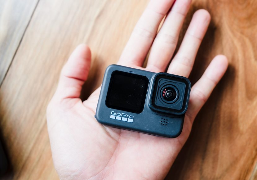 A person's hand holding a small black gopro camera.