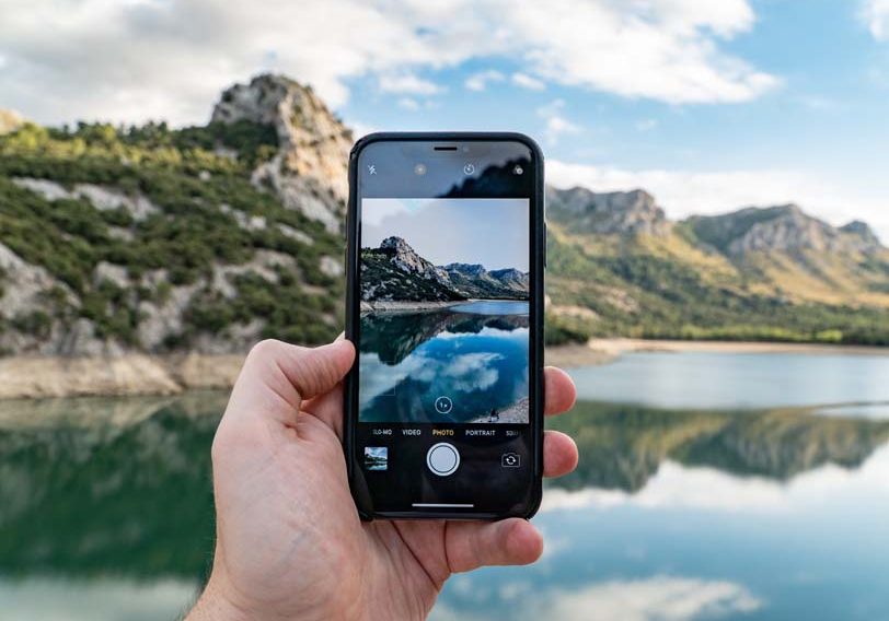 a person taking a picture of a mountain lake.