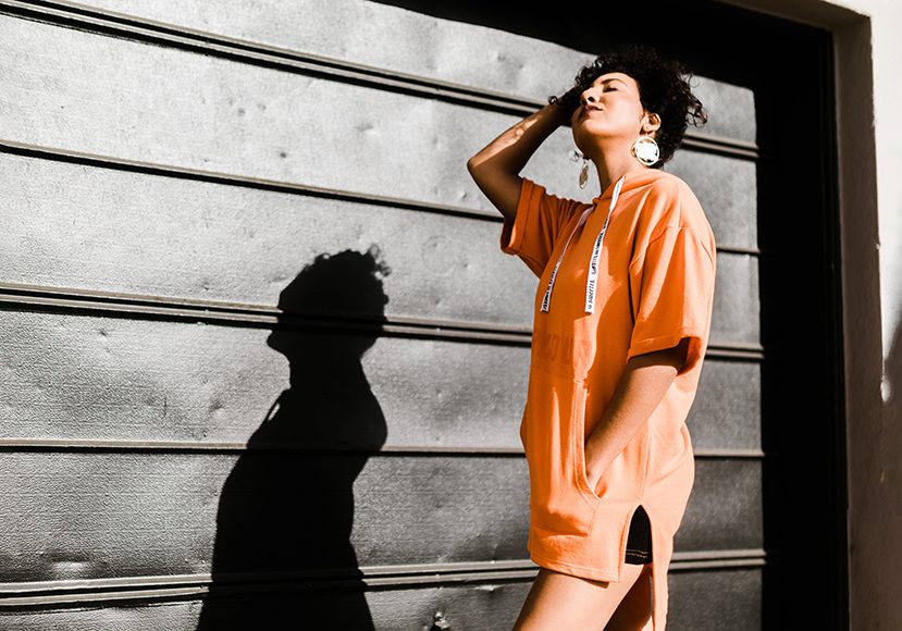 A woman in an orange t - shirt leaning against a garage door.