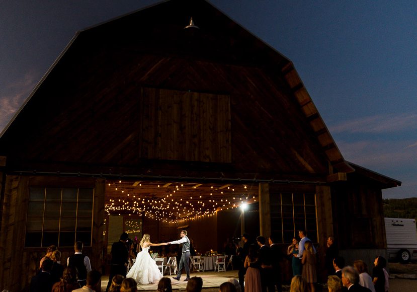 A bride and groom dance in front of a barn.