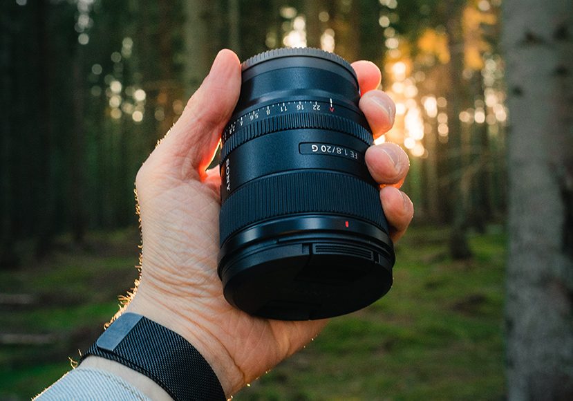 man holding camera lens in front of trees
