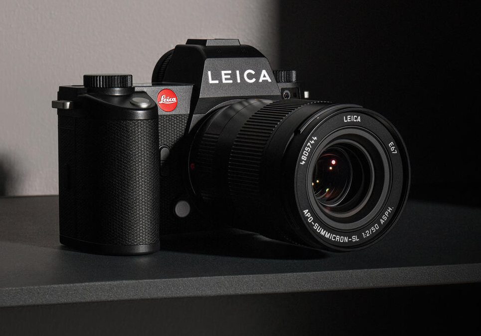 A leica camera with a lens sitting on a flat surface in a dimly lit room.