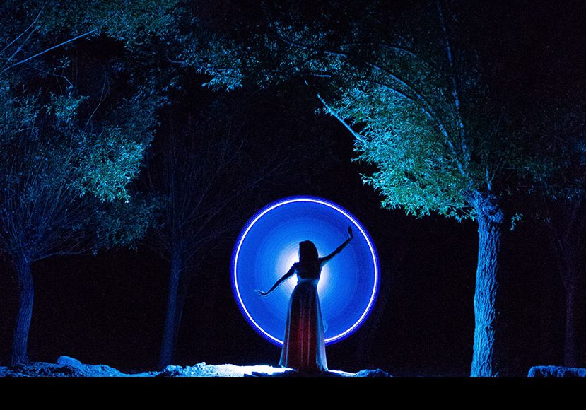 A woman in a dress standing in front of a circle of light.