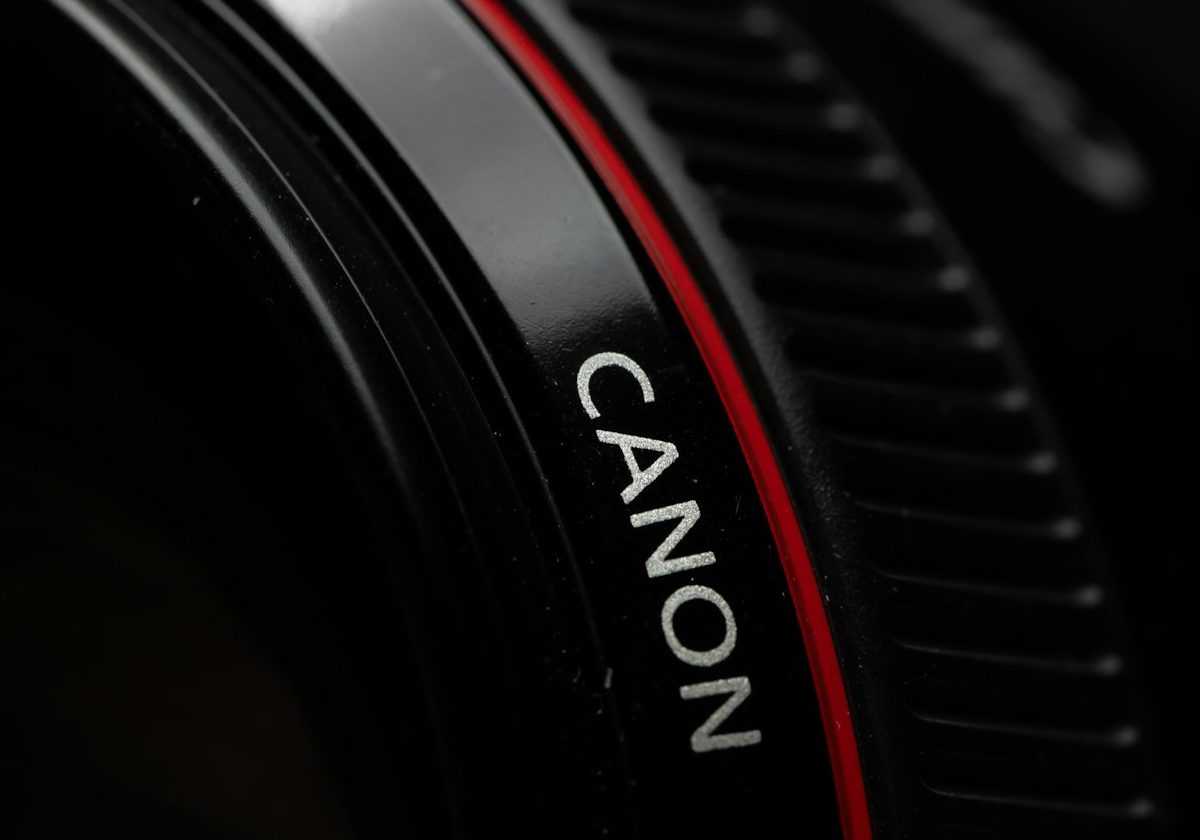 Close-up of a canon camera lens with a red accent, focusing on the brand name "canon" in white lettering against a black background.