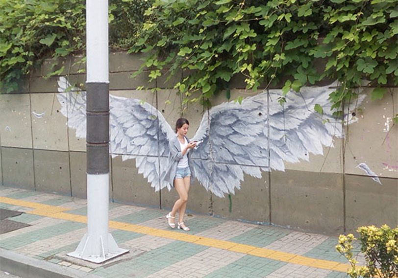 A woman is standing next to a wall with wings painted on it.