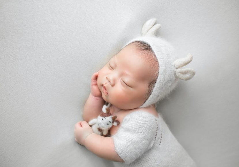 A baby sleeping in a white outfit with a teddy bear.