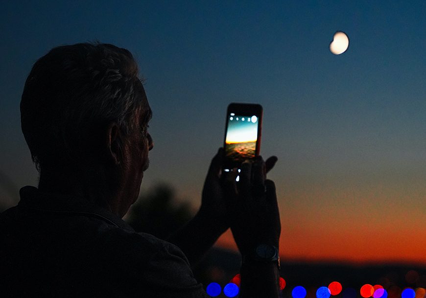 A man taking a photo of the moon with his cell phone.