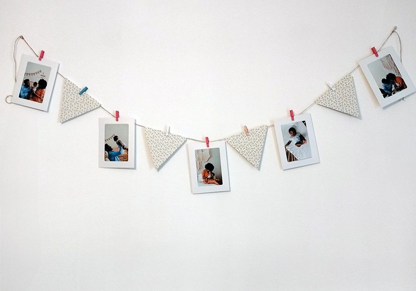 A string of photographs and patterned triangles clipped to a line against a white wall.