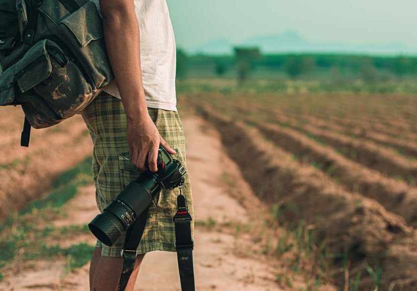 a man with a camera and a backpack on a dirt road.
