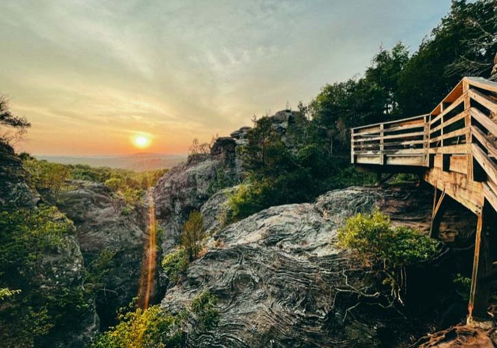 A wooden walkway leading to a cliff overlooking a sunset.