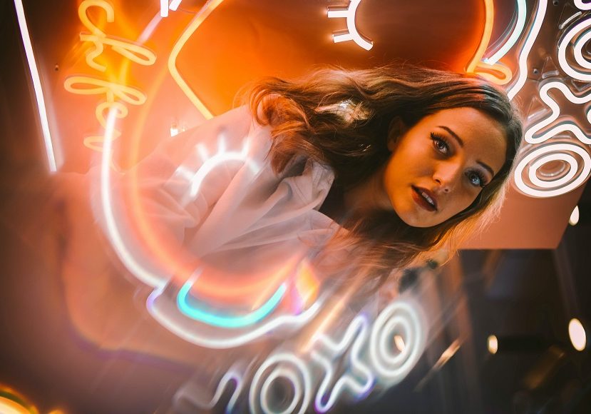 A woman is posing in front of a neon sign.
