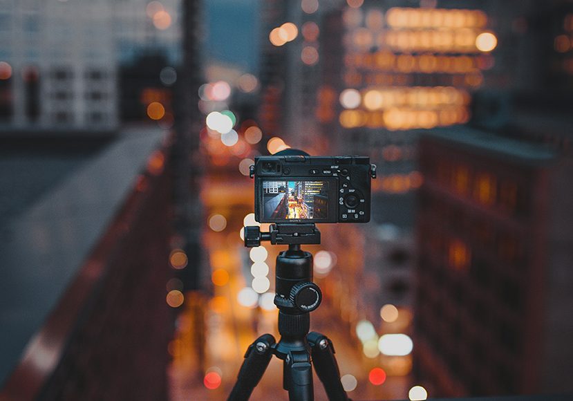 A tripod with a camera in front of a city at night.