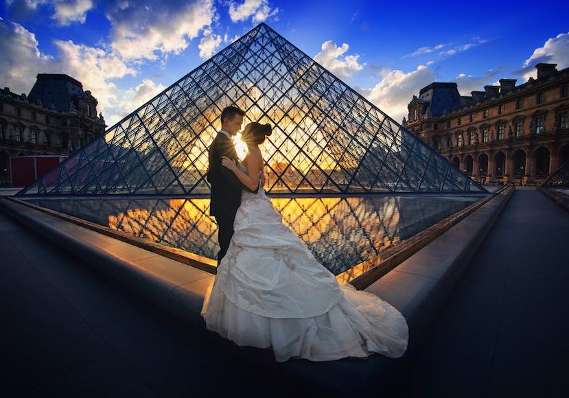 A bride and groom standing in front of a pyramid at sunset.