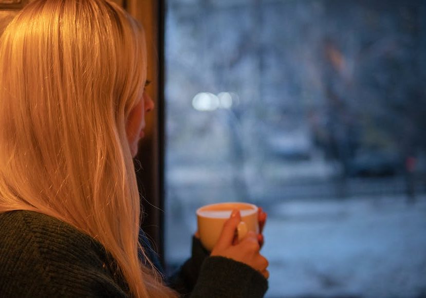 A woman drinking a cup of coffee in front of a window.