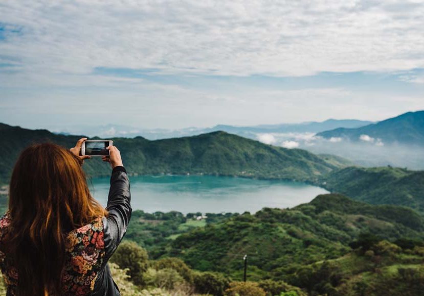 A woman taking a photo of a lake.