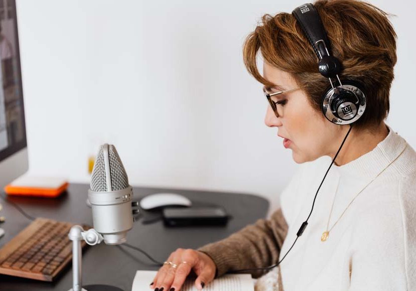 a woman sitting at a desk with headphones on by a microphone.