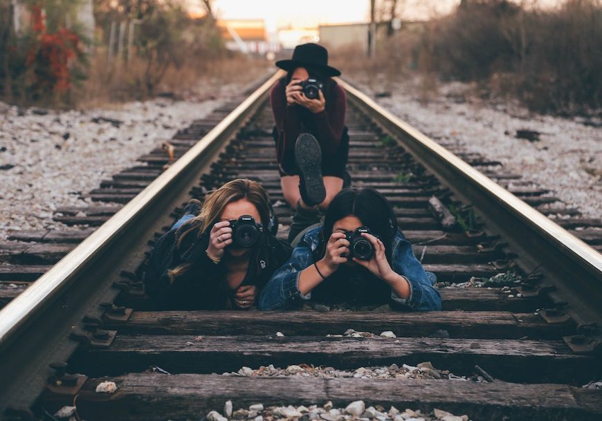 Three women taking pictures on railroad tracks.