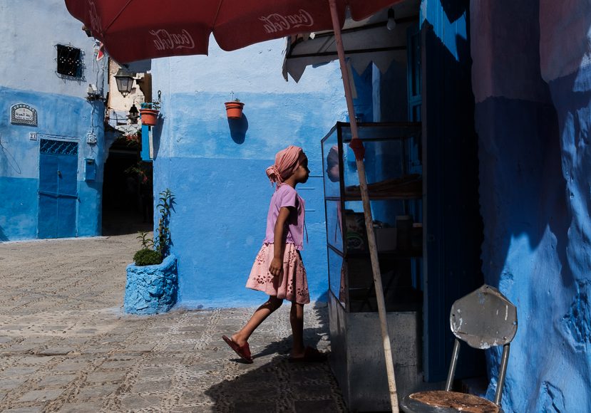 a woman walking down a street next to a blue building.